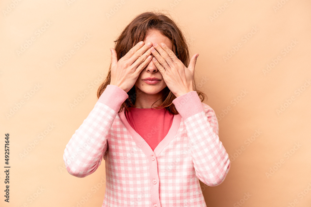 Young caucasian woman isolated on beige background afraid covering eyes with hands. Young caucasian woman isolated on beige background afraid covering eyes with hands.