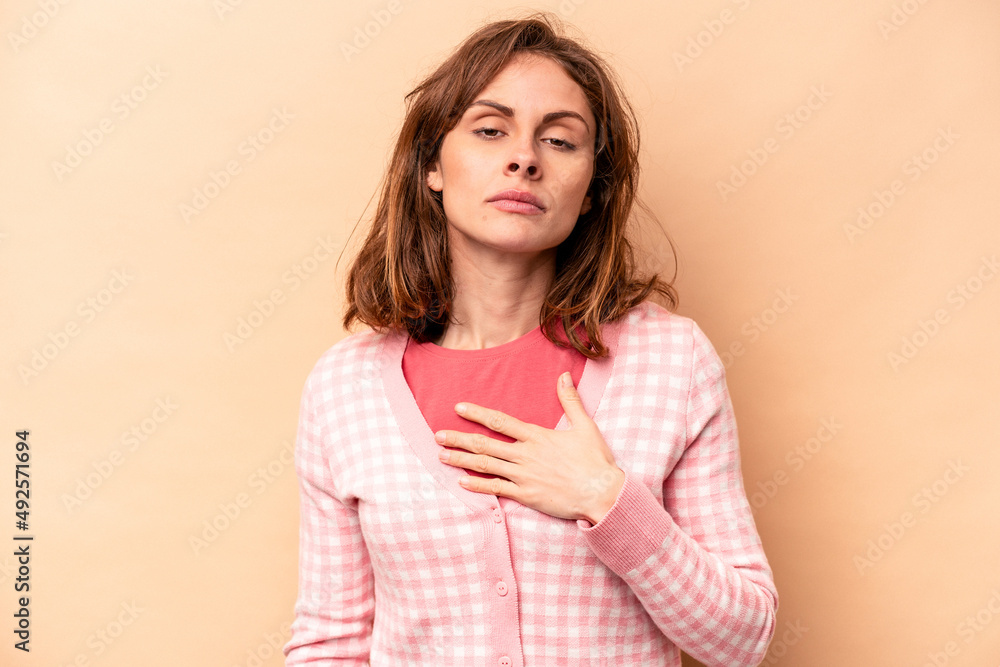 Young caucasian woman isolated on beige background taking an oath, putting hand on chest. Young caucasian woman isolated on beige background taking an oath, putting hand on chest.