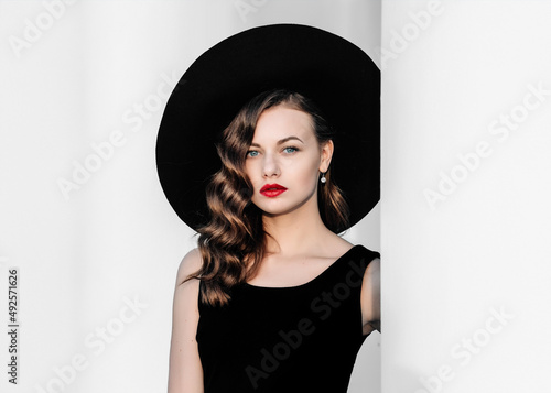 Fotografia High fashion outdoor full length portrait of elegant woman in black hat and dress standing behind white pillar