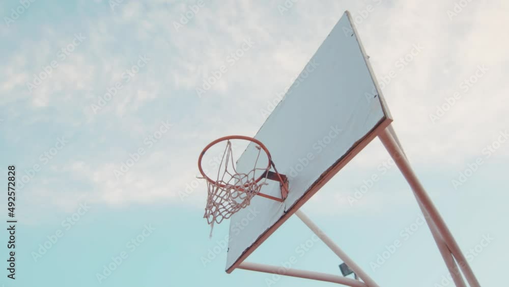 Basketball falling into net of basket outdoors against blue sky and sun - low angle Basketball falling into net of basket outdoors against blue sky and sun - low angle