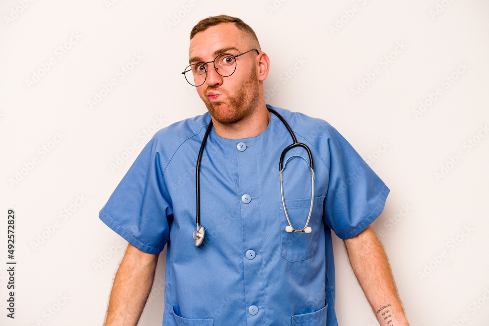 Young caucasian nurse man isolated on white background shrugs shoulders and open eyes confused. Young caucasian nurse man isolated on white background shrugs shoulders and open eyes confused.