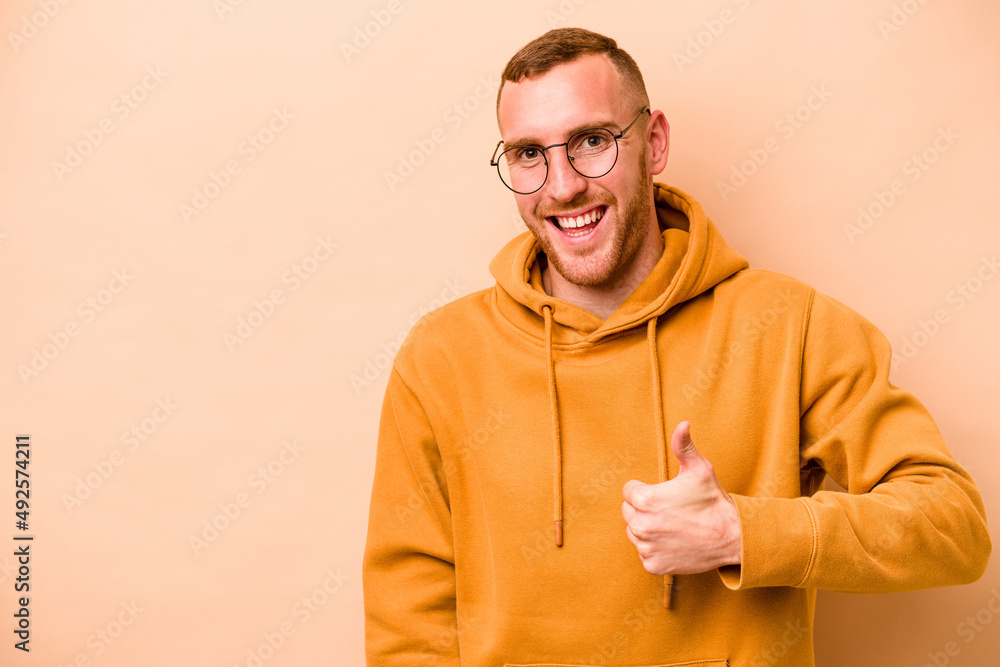 Naklejka premium Young caucasian man isolated on beige background smiling and raising thumb up
