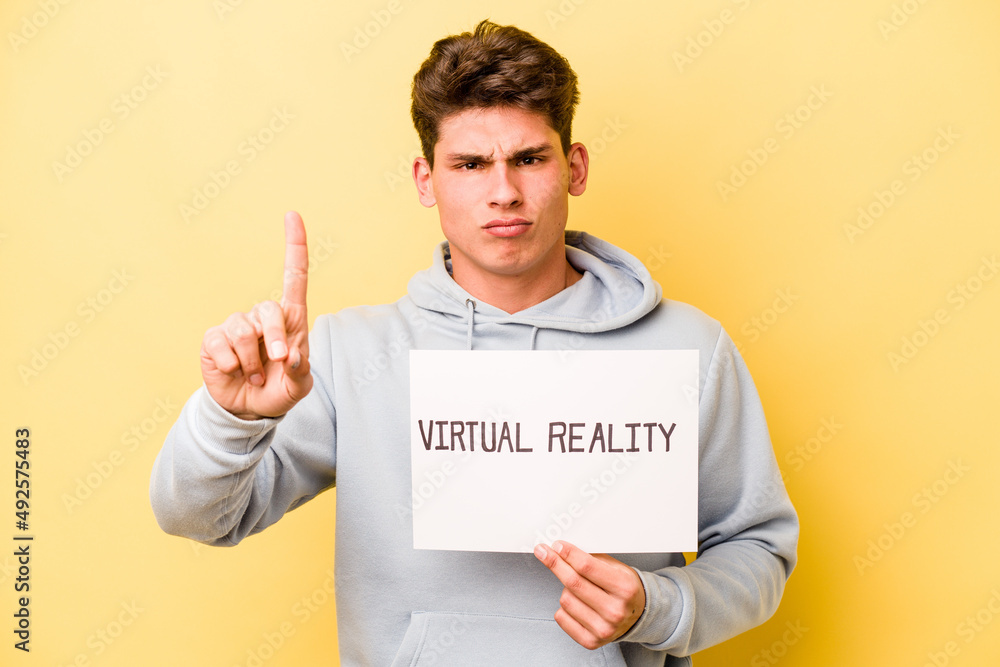 Young caucasian man holding virtual placard isolated on yellow background showing number one with finger. Young caucasian man holding virtual placard isolated on yellow background showing number one with finger.
