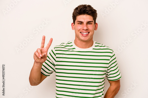 Young caucasian man isolated on white background showing victory sign and smiling broadly.