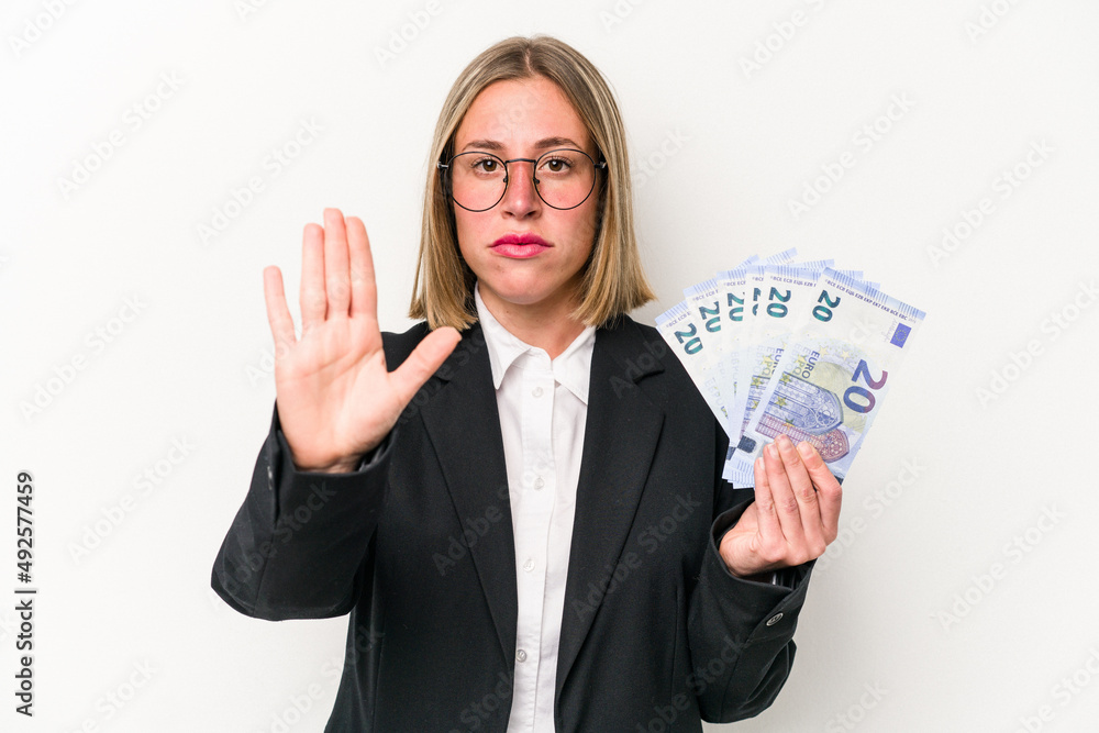 Young business caucasian woman holding banknotes isolated on white background standing with outstretched hand showing stop sign, preventing you. Young business caucasian woman holding banknotes isolated on white background standing with outstretched hand showing stop sign, preventing you.