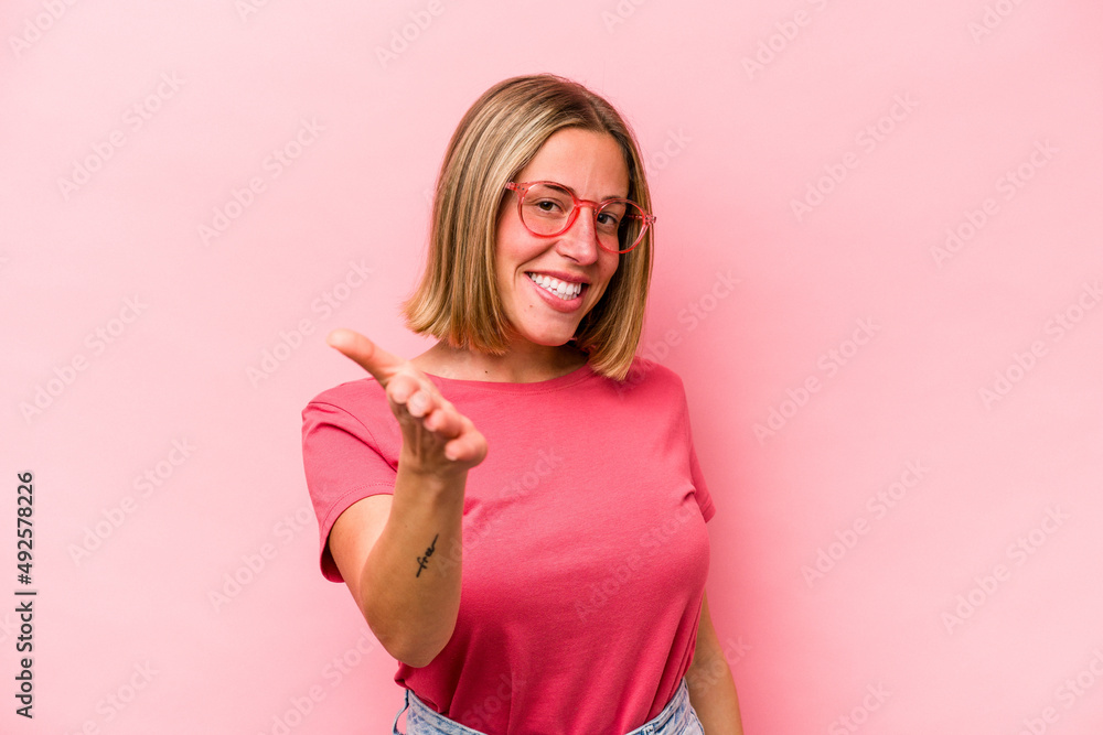Young caucasian woman isolated on pink background stretching hand at camera in greeting gesture. Young caucasian woman isolated on pink background stretching hand at camera in greeting gesture.