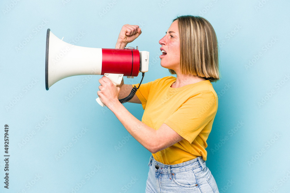 Young caucasian woman holding a megaphone isolated on blue background Young caucasian woman holding a megaphone isolated on blue background