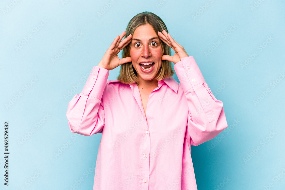 Young caucasian woman isolated on blue background receiving a pleasant surprise, excited and raising hands. Young caucasian woman isolated on blue background receiving a pleasant surprise, excited and raising hands.