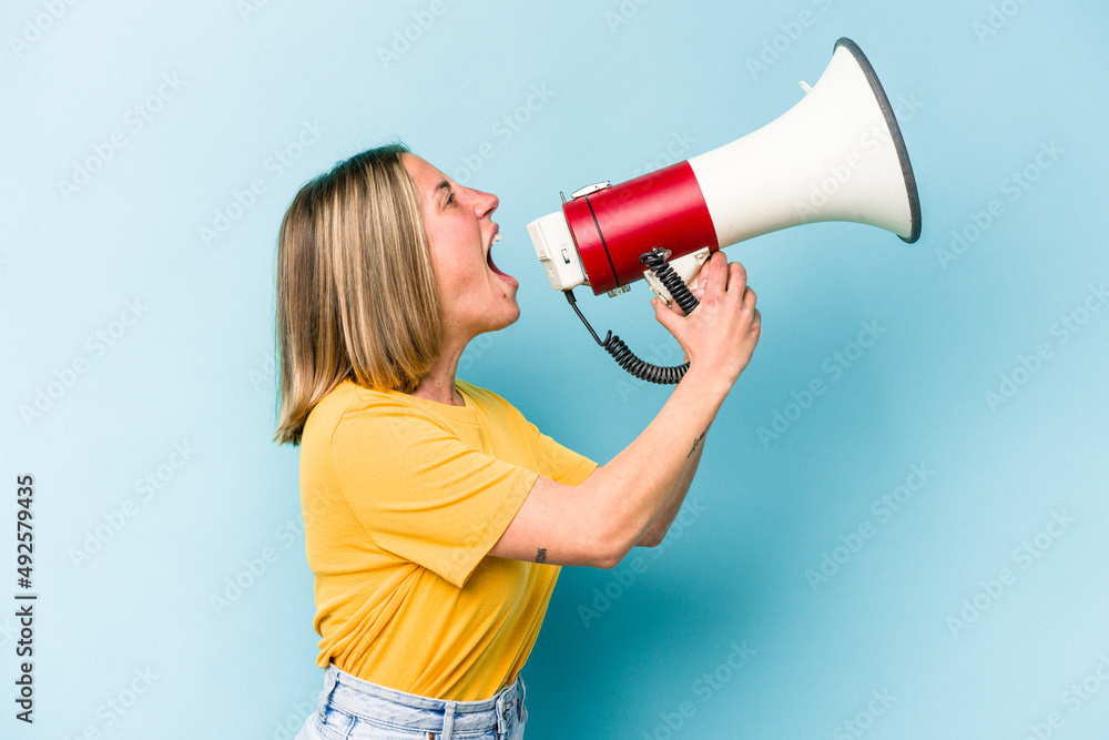 Young caucasian woman holding a megaphone isolated on blue background Young caucasian woman holding a megaphone isolated on blue background
