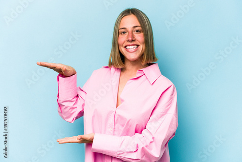 Young caucasian woman isolated on blue background holding something little with forefingers, smiling and confident.