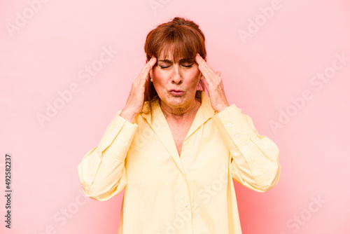 Middle age caucasian woman isolated on pink background having a head ache, touching front of the face.