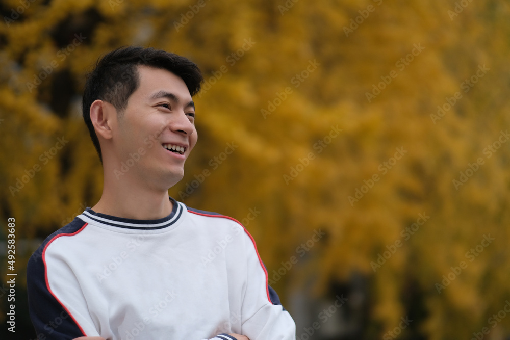 portrait of happy Asian young man and blurred yellow ginkgo biloba tree in autumn. Smiling side face portrait of happy Asian young man and blurred yellow ginkgo biloba tree in autumn. Smiling side face