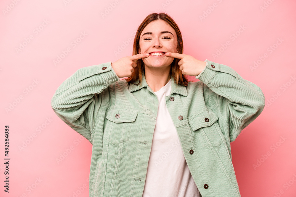 Young caucasian woman isolated on pink background smiles, pointing fingers at mouth. Young caucasian woman isolated on pink background smiles, pointing fingers at mouth.