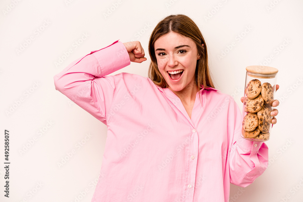 Young caucasian woman holding cookies jar isolated on white background raising fist after a victory, winner concept. Young caucasian woman holding cookies jar isolated on white background raising fist after a victory, winner concept.