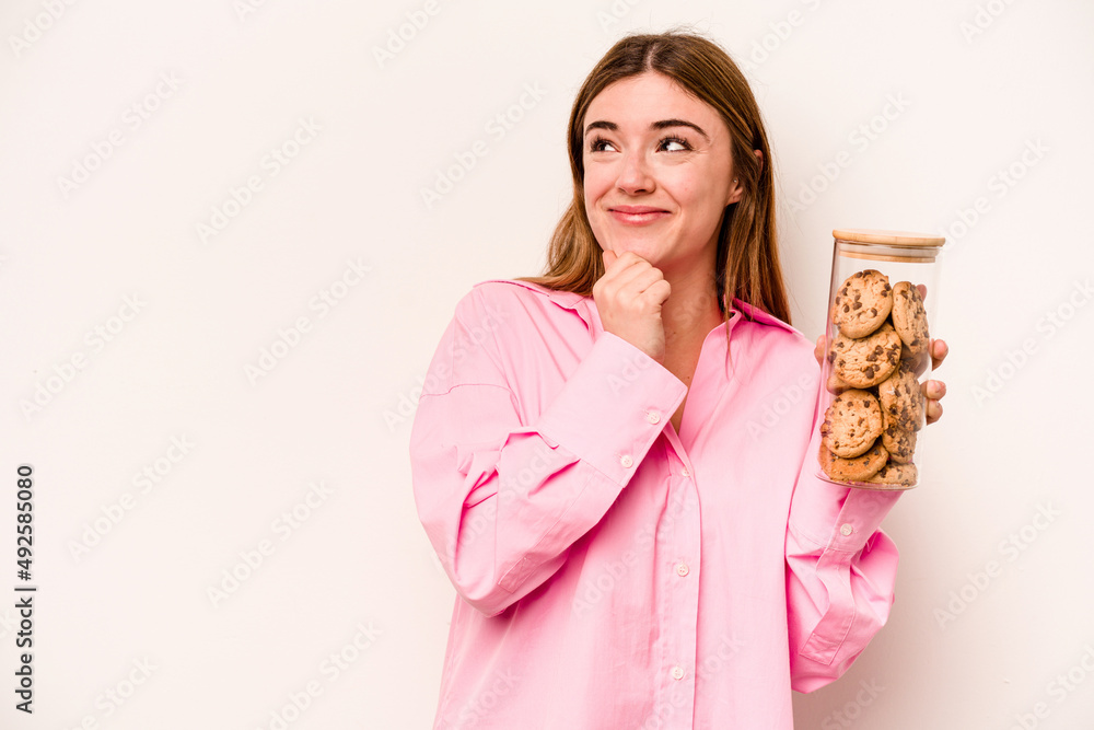 Young caucasian woman holding cookies jar isolated on white background looking sideways with doubtful and skeptical expression. Young caucasian woman holding cookies jar isolated on white background looking sideways with doubtful and skeptical expression.
