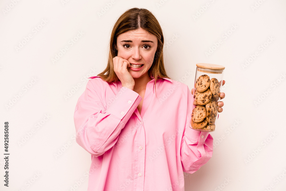Young caucasian woman holding cookies jar isolated on white background biting fingernails, nervous and very anxious. Young caucasian woman holding cookies jar isolated on white background biting fingernails, nervous and very anxious.