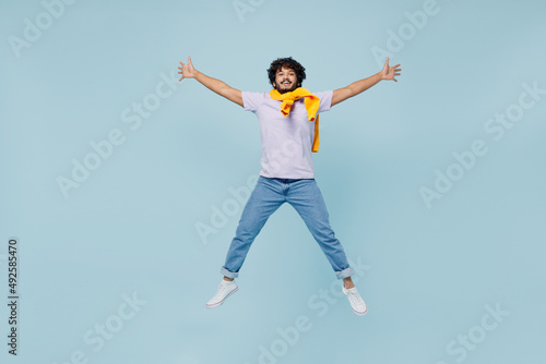 Full size body length cheerful happy young bearded Indian man 20s years old wears white t-shirt raise up spreading hands looking camera isolated on plain pastel light blue background studio portrait.