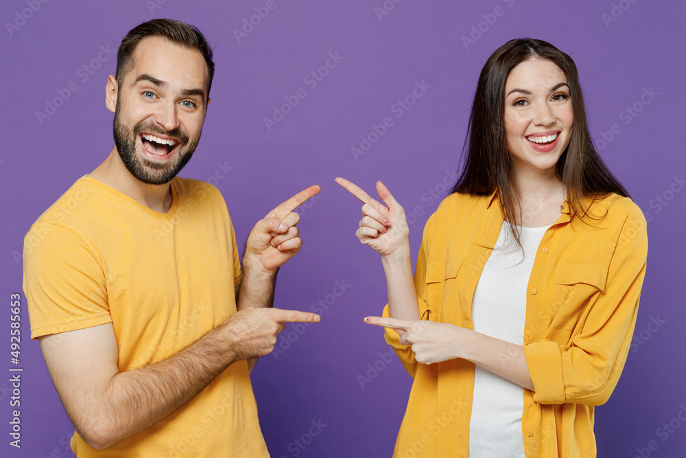 Young smiling happy cheerful fun cool couple two friends family man woman 20s together wear yellow casual clothes point index finger on each other isolated on plain violet background studio portrait. Young smiling happy cheerful fun cool couple two friends family man woman 20s together wear yellow casual clothes point index finger on each other isolated on plain violet background studio portrait.