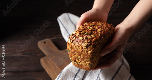 Homemade crusty loave of bread with pumpkin seeds on wooden background. Dark mood. Baker holding fresh bread in the hands. Traditional techniques, innovating bread, slow carb baking photo