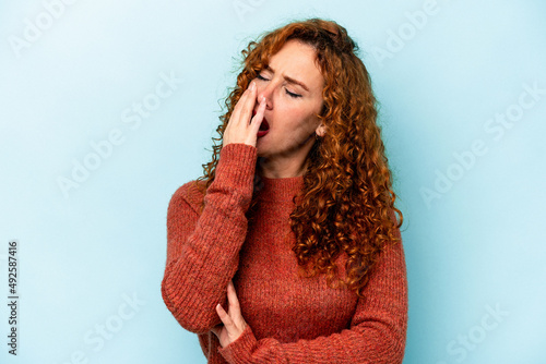 Young ginger caucasian woman isolated on blue background yawning showing a tired gesture covering mouth with hand.