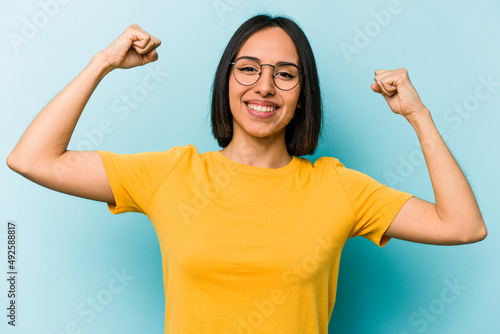 Young hispanic woman isolated on blue background showing strength gesture with arms, symbol of feminine power