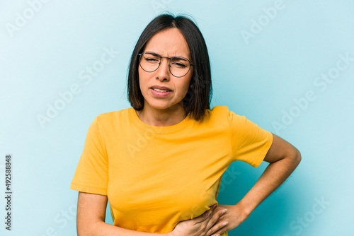 Young hispanic woman isolated on blue background having a liver pain, stomach ache.