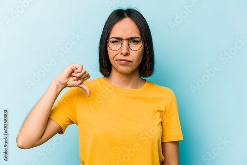 Young hispanic woman isolated on blue background showing thumb down, disappointment concept.