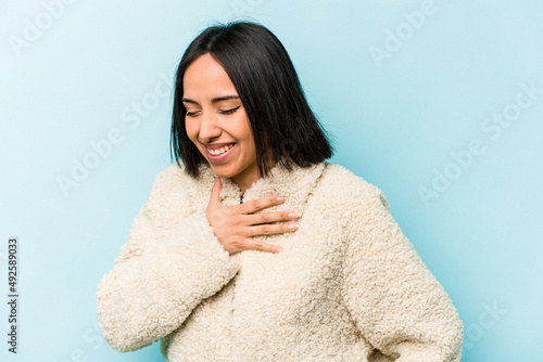 Young hispanic woman isolated on blue background laughing keeping hands on heart, concept of happiness.