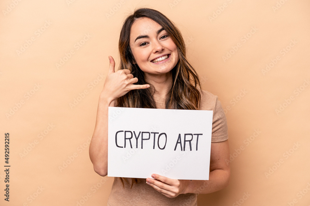 Young caucasian woman holding a crypto art placard isolated on beige background showing a mobile phone call gesture with fingers. Young caucasian woman holding a crypto art placard isolated on beige background showing a mobile phone call gesture with fingers.