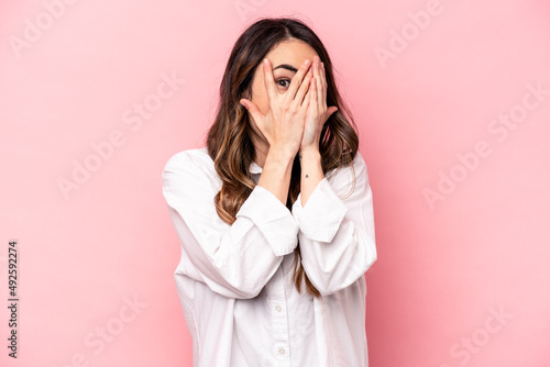 Young caucasian woman isolated on pink background blink through fingers frightened and nervous. © Asier