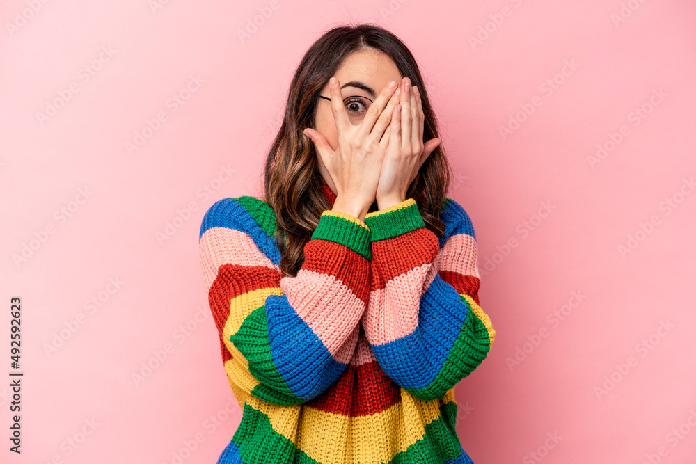 Young caucasian woman isolated on pink background blink through fingers frightened and nervous. Young caucasian woman isolated on pink background blink through fingers frightened and nervous.