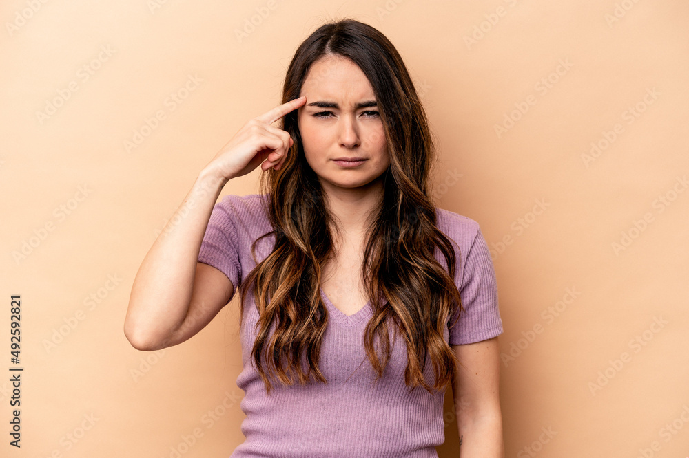 Young caucasian woman isolated on beige background pointing temple with finger, thinking, focused on a task. Young caucasian woman isolated on beige background pointing temple with finger, thinking, focused on a task.
