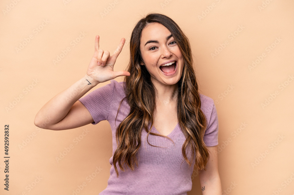 Young caucasian woman isolated on beige background showing a horns gesture as a revolution concept. Young caucasian woman isolated on beige background showing a horns gesture as a revolution concept.
