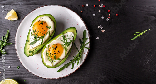 Avocado baked with eggs, fresh arugula, ground pepper on dark background, top view