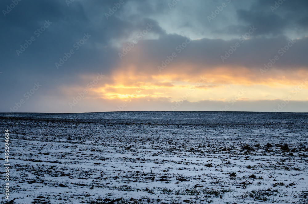 Winter evening. Beautiful multicolored sunset in the sky over a snow-covered field