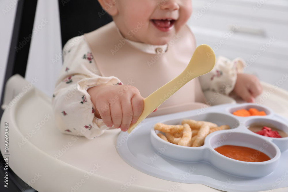 Little baby eating food in high chair indoors, closeup Little baby eating food in high chair indoors, closeup