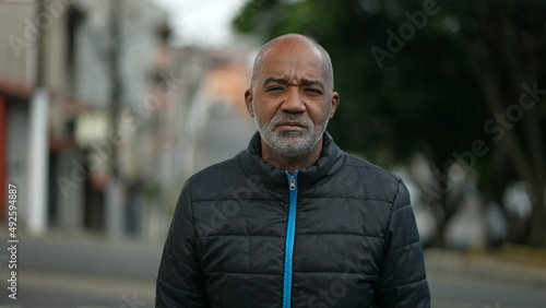 Portrait of a serious senior black man standing outside in street looking at camera