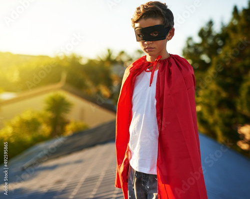 Watching over his neighbourhood. Portrait of a young boy in a cape and mask playing superhero outside.