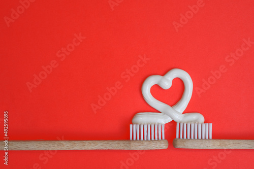 Zwei Zahnbürsten aus Holz mit Herz aus Zahnpasta, roter Hintergrund, horizontal