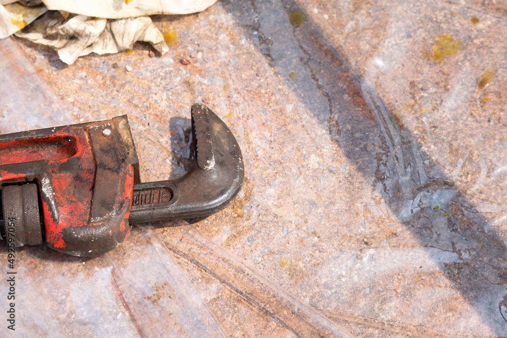 A dirty adjustable pipe wrench is placed on ground at construction working area. Industrial equipment part photo. Close-up.