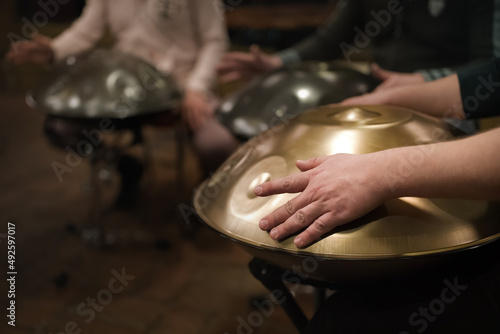 A musician's hand playing the handpan with other people. Handpan is a term for a group of musical instruments that are classified as a subset of the steelpan.  photo