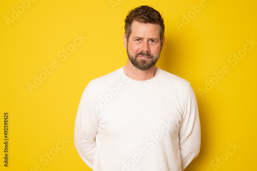 Cheerful bearded man in a white sweater standing isolated over yellow background.