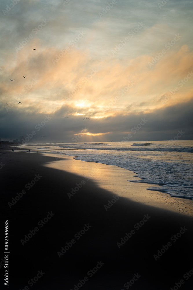 Seagulls soar as the sun breaks through a storm cloud over the atlantic ocean