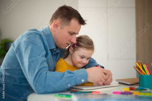 Father with his little daughter with Down syndrome learning at home.