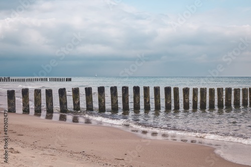 Cloudy seaside landscape. Sandy beach with wooden logs in the sea.