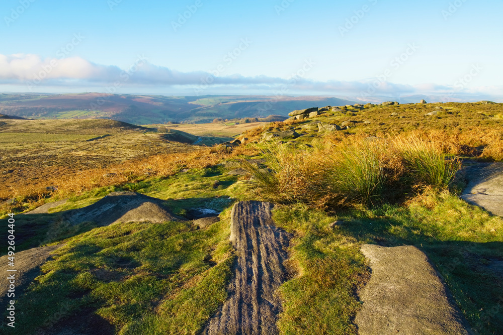 Weathered rocks lay among the grass and heather of Higger Tor in the autumn sun