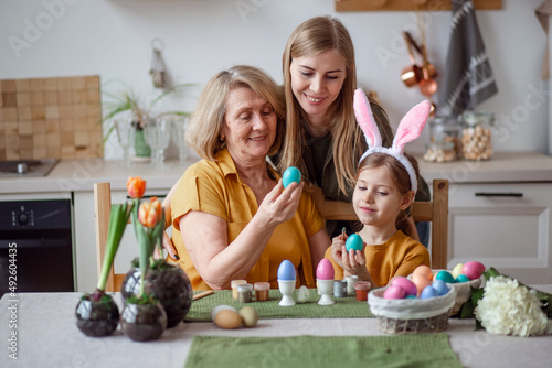 Happy easter family elderly grandmother and young woman mother blonde with little daughter with rabbit ears are preparing for the holiday to paint eggs