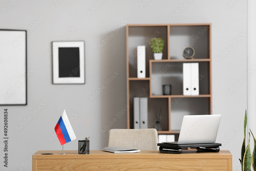 Workplace with modern laptop, notebook, stationery holder and Russian flag in light room Workplace with modern laptop, notebook, stationery holder and Russian flag in light room