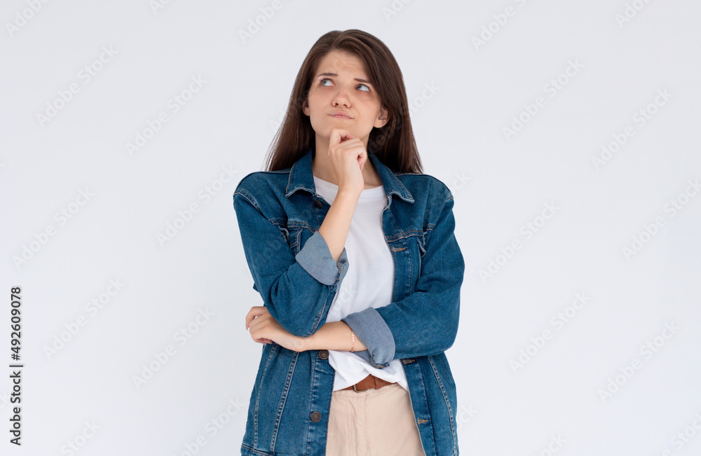 Close up portrait of pretty confident thoughtful girl, holding hand near the face, looking seriously up, standing over grey background with copy space Close up portrait of pretty confident thoughtful girl, holding hand near the face, looking seriously up, standing over grey background with copy space