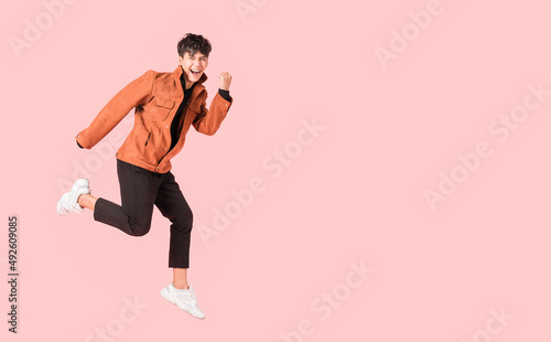 Happy handsome Asian man in fashionable clothing and jumping doing winner gesture isolated on pink background.